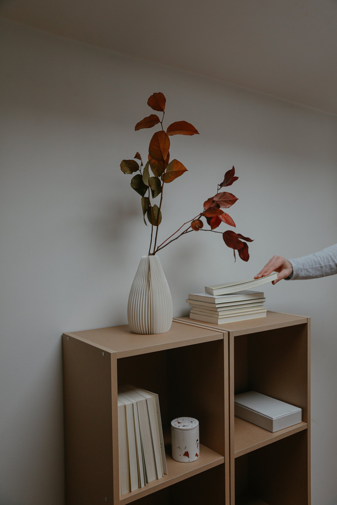 Photo of a Person Getting a Book Near a White Vase